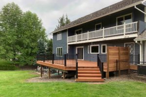 The backside of a blue house with a new deck on the first floor with black metal railing.