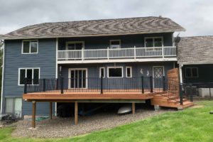 The backside of a blue house with a new deck on the first floor with black metal railing.