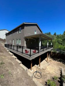 Brown house with completed deck on two sides with railing and patio cover.