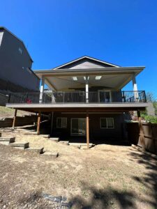 Brown house with completed deck on two sides with railing and patio cover.