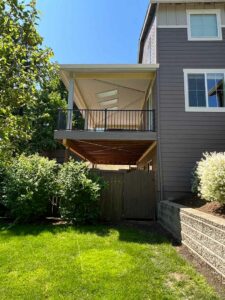 Brown house with completed deck on two sides with railing and patio cover.